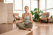 © pressmaster - Young active blond woman crossing legs while meditating on the floor at home