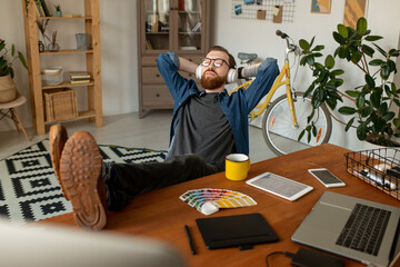 Wall Mural - Young relaxed freelance designer with his legs on table listening to music
