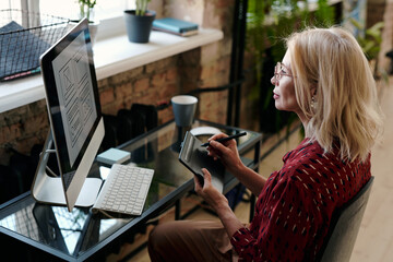 Blond mature mobile application developer sitting in front of computer monitor