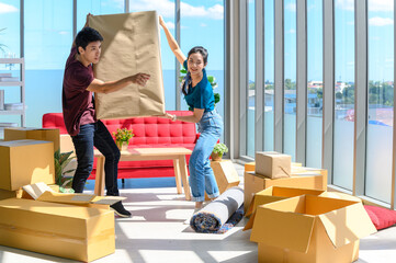 young asian couple smiling and enjoy when they carrying big cardboard box while relocation into new home on moving day, celebrating moving to new home concept