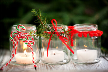 Cozy handmade holiday home decor. Christmas decoration with candles in glass jars decorated red ribbon.