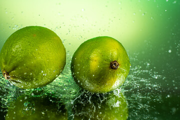 two whole limes with splashing water on gradient background