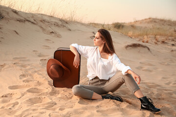 Poster - Beautiful fashionable young woman with suitcase in desert