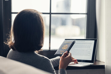 Woman  holding passport filling visa application form on the laptop. Online and home work concept.