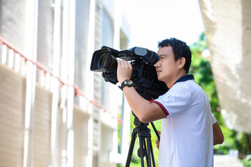 Young cameraman using a professional camcorder outdoor filming news with blur background.