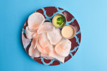 Rice crispy chips sprinkled with paprika and served with two different kinds of sauce on a colorful plate.