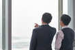 © imtmphoto - rear view of two asian businessmen standing in front of window talking discussing chatting conversing in office