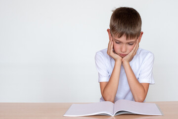 Back to school. Thinking child boy looking in a notebook or book, sitting at the table and doing homework