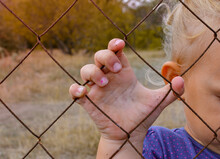 The Child Holds An Iron Fence With His Hand. Sad Child. Cruelty To Children.