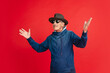 Greeting. Portrait of senior man in stylish eyewear and hat isolated on red studio background. Tech and joyful elderly lifestyle concept. Trendy colors, forever youth. Copyspace for your ad.