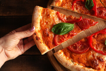 .A piece of pizza is taken by hand. Wood background. Side view