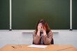 Sad teacher sits in a school classroom, copy space