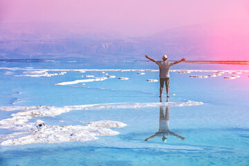 Fototapete - Silhouette of a man with hands in the air  walking on Dead Sea salt shore at sunrise