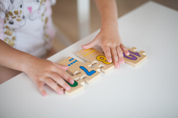 Hands of preschooler child girl playing educational games with wooden mathematical multicolored figures preparing for school in kindergarten while sitting at table. Back to school concept.