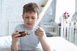 © Chepko Danil - Sick child boy drinking cough syrup sitting on bed at home, teen recover from flu.