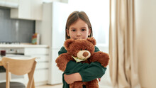 A Little Girl Embracing A Fluffy Brown Teddy Bear Looking Into A Camera