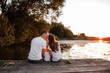© Andriy Medvediuk - Young parents and their little son sitting on the wooden pier near the lake, at sunset on summer day.