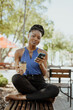 © F8  \ Suport Ukraine - Young african woman sitting on bench drinking coffee and using phone outdoors