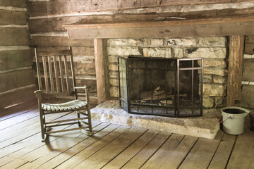 Empty Rocking Char. Empty chair by a fireplace inside a rustic pioneer log cabin. This is a historical structure located within a state park and not a private property or residence. 