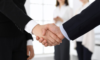 Businessman and woman shaking hands with colleagues at the background. Handshake at meeting in office. Concept of success in business