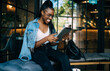 © BullRun - Cheerful dark skinned woman in trendy wear and spectacles having fun on free time in cafe watching videos on modern digital tablet, positive young african american female browse web page read book