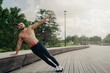 © VK Studio - Handsome serious man stands in side plank, has perfect body constitution, poses with naked chest outdoors, keeps arm raised, trains for being healthy, dressed in sport trousers and sneakers.
