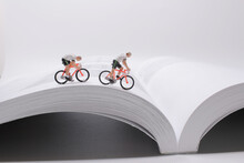 The Mini People,  Small Figures Cycling On Open Book