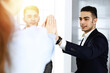 © Iryna - Business people group showing teamwork, joining hands and giving five to each other in sunny office