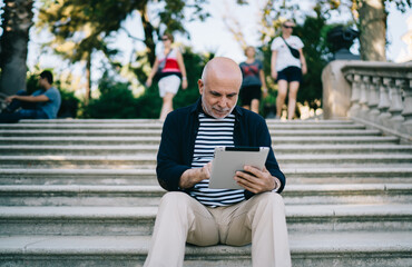Focused aged man using tablet on steps in park