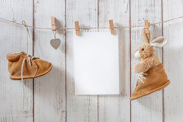 children's shoes for the first steps, small brown shoes in a retro style hang on clothespins with a soft toy and a blank sheet of paper, free space, childhood concept