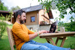 © Halfpoint - Side view of man with laptop working outdoors in garden, home office concept.