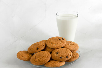 Milk in a glass, next to oatmeal cookies with chocolate chips. White marble background. Selective focus. Copy space. Banner
