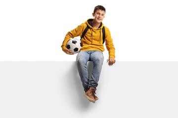 Wall Mural - Teenager boy holding a soccer ball and sitting on a white panel board