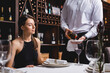 © LIGHTFIELD STUDIOS - Selective focus of sommelier pouring wine in glass near young woman in restaurant