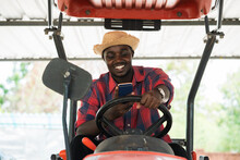 African Farmer Using Smartphone And Driving Tractor In Farm During Harvest In Countryside. Agriculture Or Cultivation Concept