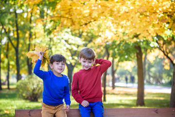 Wall Mural - happy friends, schoolchildren having fun in autumn park among fallen leaves