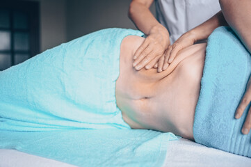 Young unrecognizable woman lying on massage table and enjoying therapeutic massage. Body care, losing weight concept. Hands masseur massage therapist doing anti-cellulite massage in spa clinic.