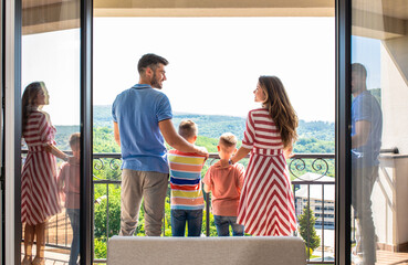 Rear view of smiling family of four in the hotel room standing at terrace.