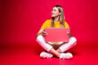 © dianagrytsku - Happy young woman sitting on the floor with crossed legs and using laptop on red background.