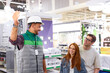 © Roman - warehouse worker and customers in the department of light bulbs and chandeliers, affable worker in uniform consult customers about light bulbs