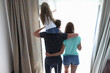 © H_Ko - Family dad mom daughter stand with their backs hugged and look out window. Mutual understanding and support in the family concept