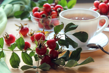 Rosehip branch with fruit on the background of a Cup and dishes with rosehip, close - up-the concept of using a medicinal decoction for colds