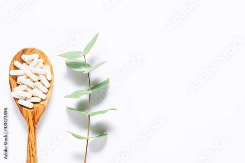 Fotomural Collagen capsules in the wooden spoon and aromatic eucalyptus twig on white background