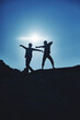 © Nicolaos - Dark silhouettes of a young couple of a guy and a girl of travelers on the top of the mountain indulge and rejoice against the background of the sun