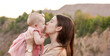 © lunarts_studio - Mom holds a child in her arms and kisses him gently on the cheek outdoor. Mom and daughter. Family concept.