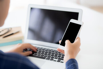 Wall Mural - hand of young man working with laptop computer and smartphone mockup on desk at home, notebook and p