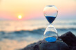 © oleg_chumakov - Hourglass with sand standing on rock. Sunset over sea and nature landscape. Running of time and relax idea, copy space