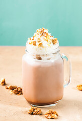 Wall Mural - Winter hot dark chocolate or cocoa drink with whipped cream and crushed walnuts in glass jar, beige table, copy space