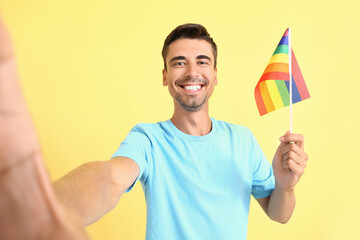 Wall Mural - Young man with LGBT flag taking selfie on color background