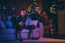 Full Length Photo Of Elf Play Sit Comfort Couch Play Win Video Game Raise Fist In House Indoors With Christmas X-mas Evening Lights
